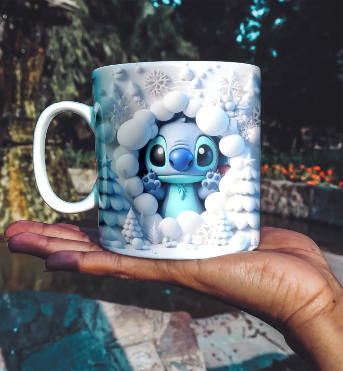 Mão segurando caneca branca estampada com criatura azul entre neve e árvores.