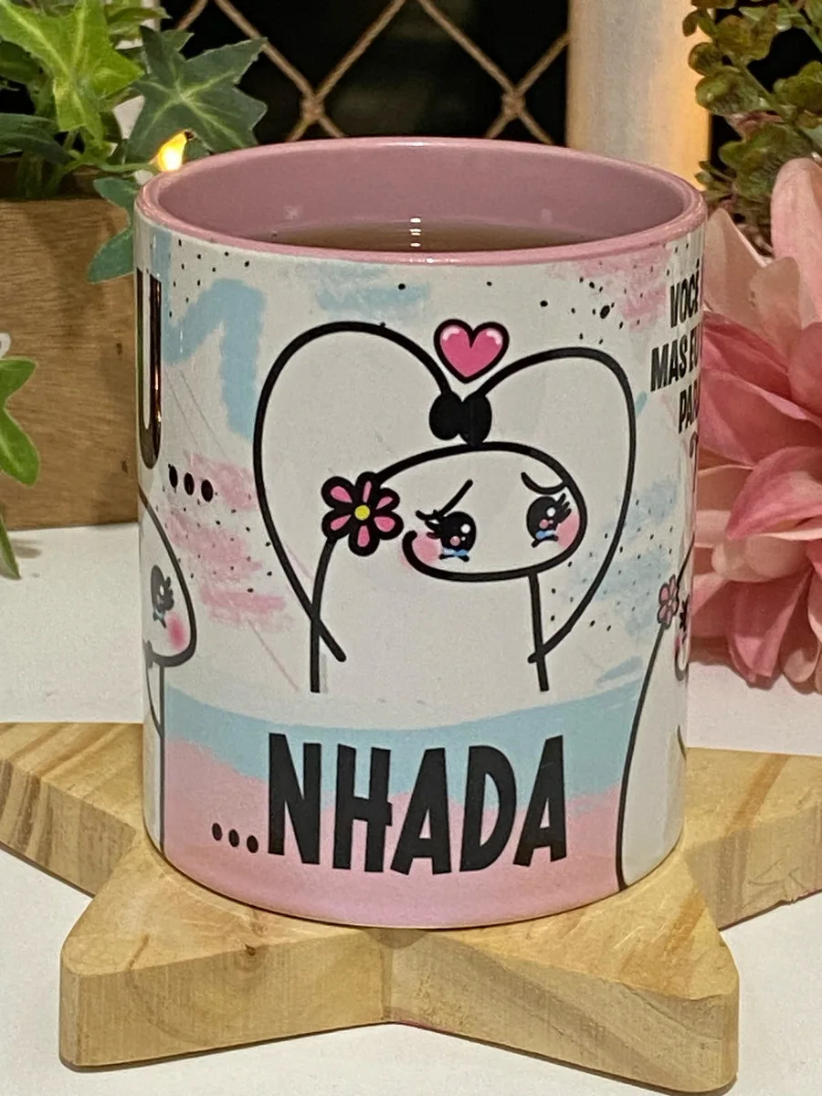 Caneca rosa com estampa de desenho e texto sobre suporte de madeira.