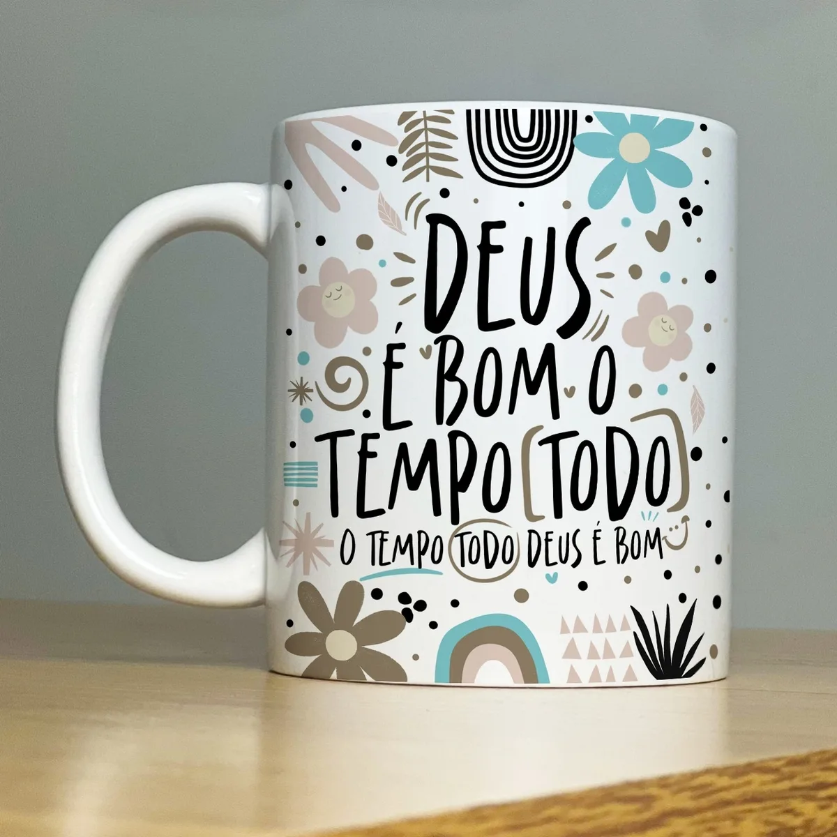 Caneca branca com frase religiosa e flores sobre mesa de madeira