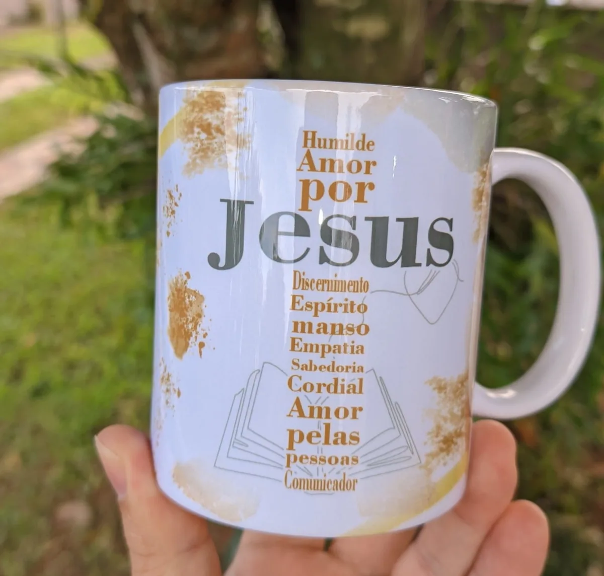 Mão segurando uma caneca branca com estampa de texto e fundo dourado suave.