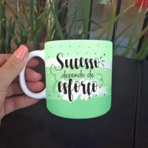 Mão feminina segura caneca verde clara com frase motivacional.