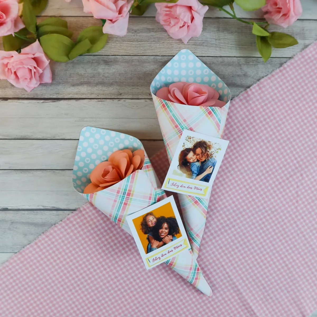 Dois cones de papel estampados contendo flores artificiais e fotos de mães com filhos.