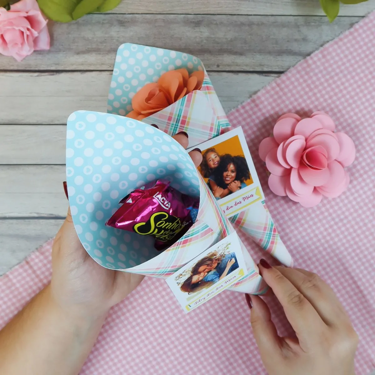 Mãos segurando cones de papel decorados com fotos para presente de dia das mães.