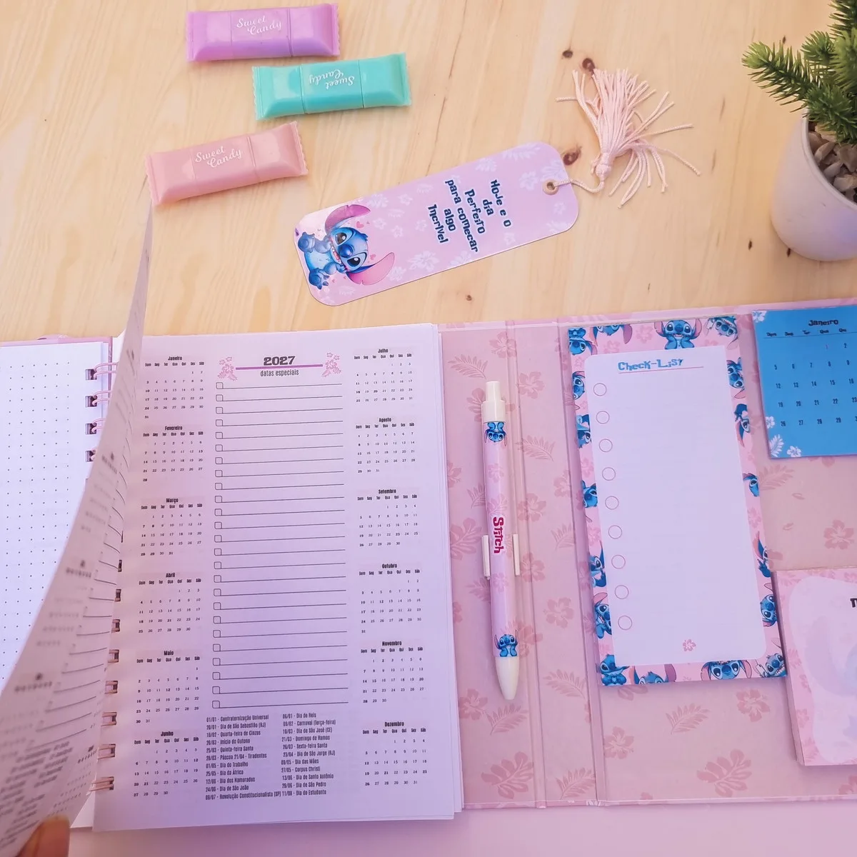 Agenda aberta sobre mesa de madeira com caneta, marca-páginas e pequenos blocos coloridos.