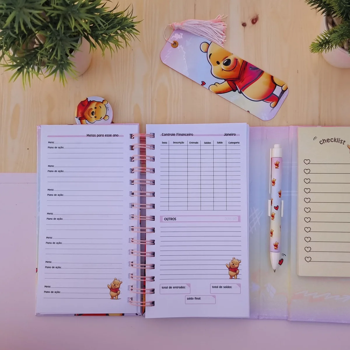 Caderno aberto com páginas organizadoras, marca-página, caneta e bloco de notas em mesa.
