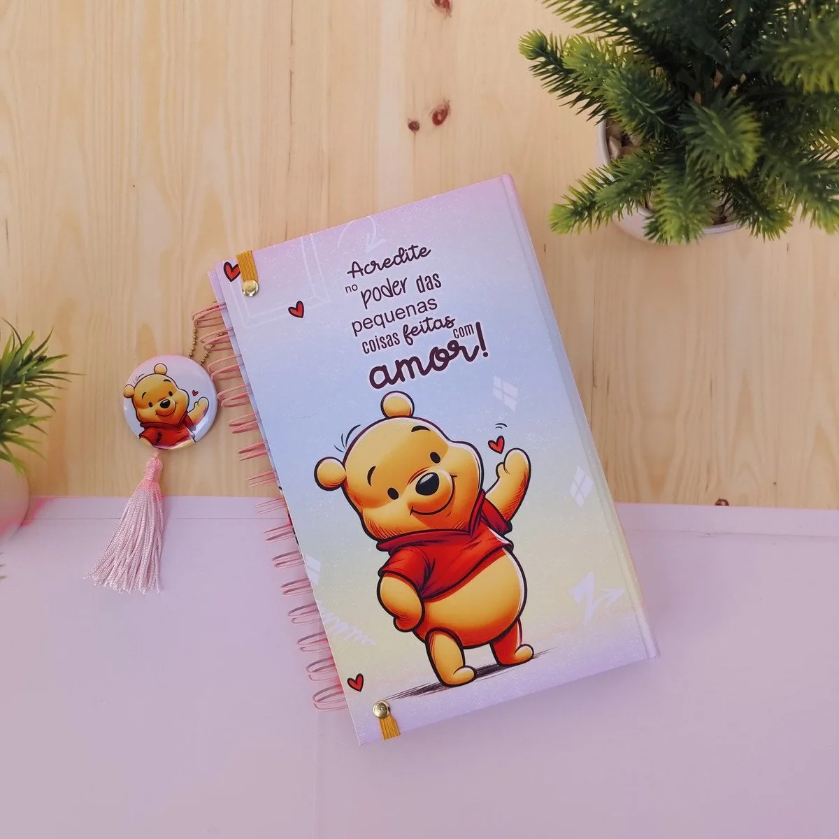 Caderno espiral ilustrado com urso amarelo e frase motivacional em fundo claro.
