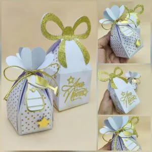 Caixas de papel decoradas em branco e dourado com laços brilhantes e estrelas.