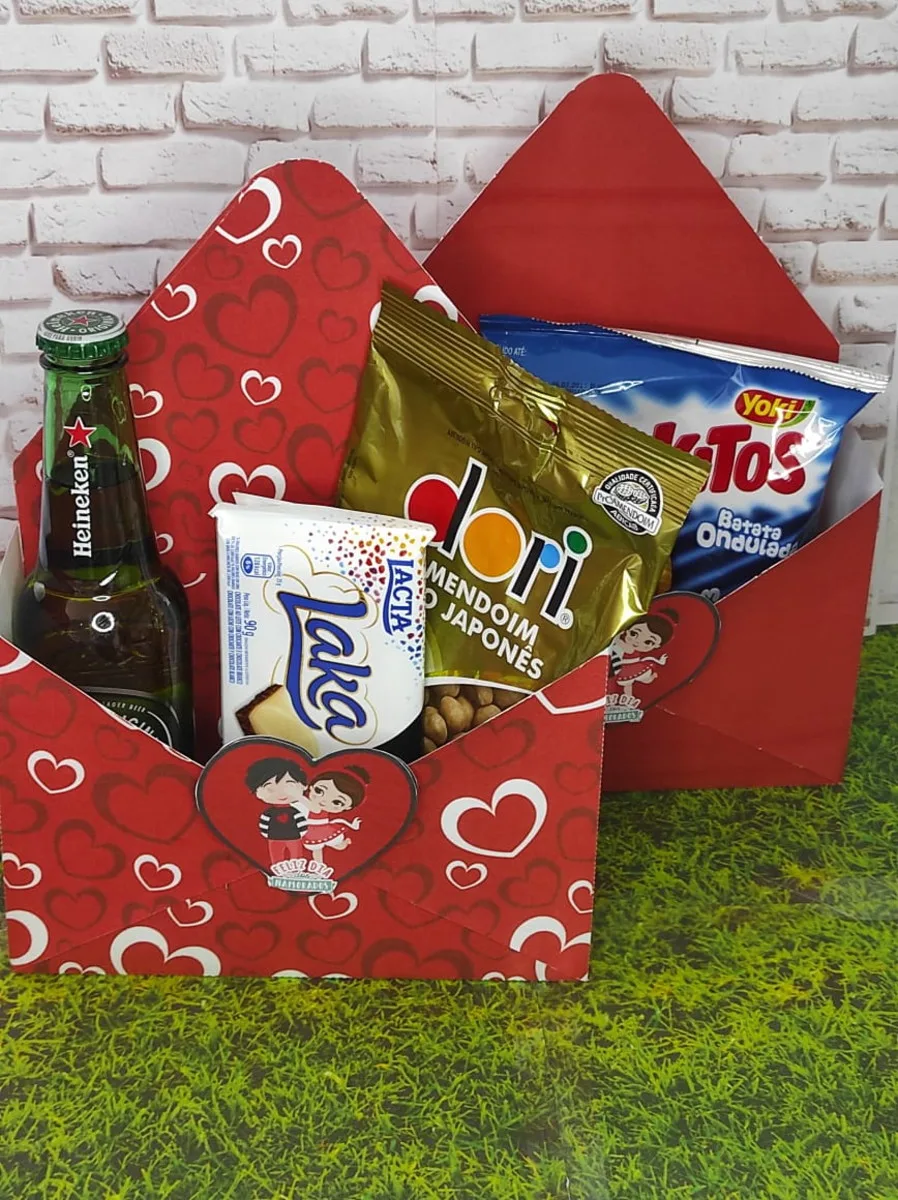 Cesta vermelha decorada com corações contendo garrafa de cerveja, chocolates e salgadinhos.