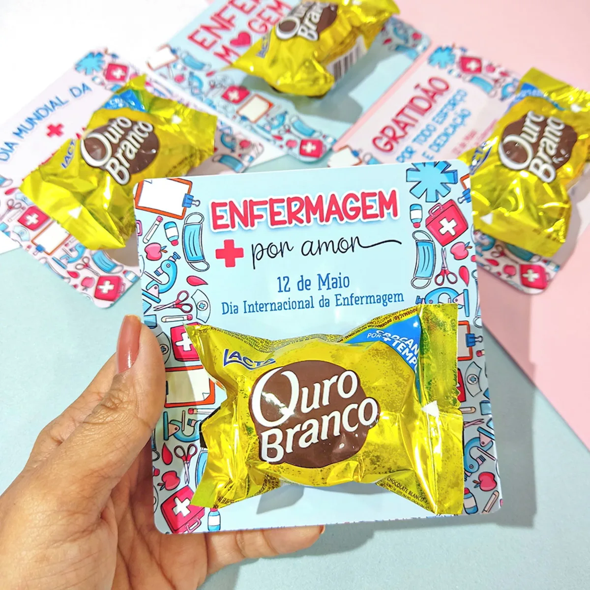 Card Bombom Dia Dia do Enfermeiro 4 Mão segura cartão com tema de enfermagem e doces dourados sobre fundo colorido