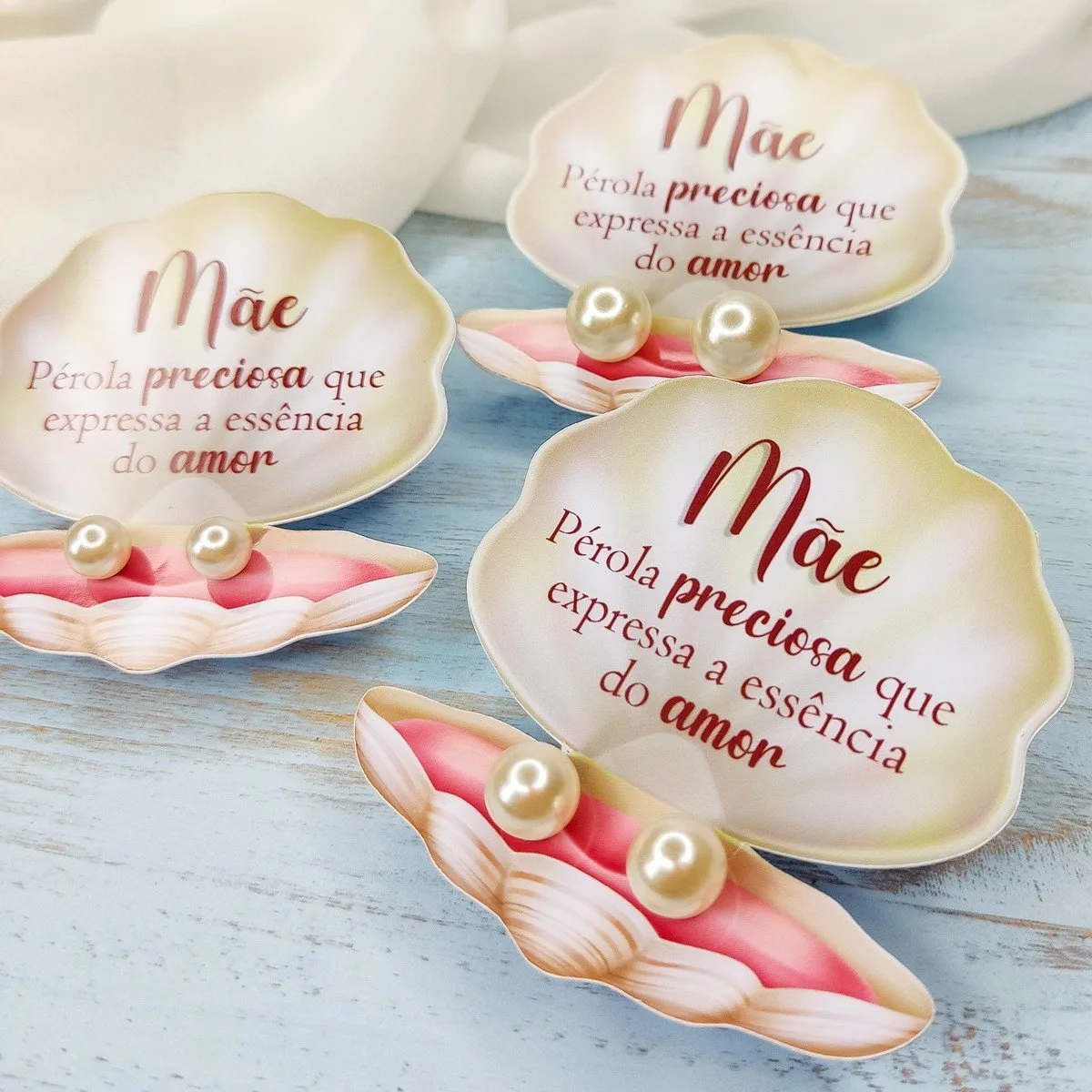 Conchas abertas com pérolas e texto Mãe em fundo claro de tecido e madeira