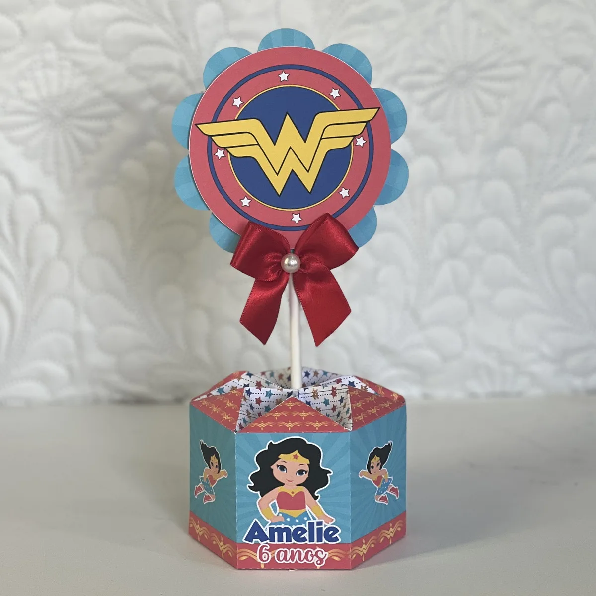 Centro de mesa hexagonal personalizado com tema de super-heroína e laço vermelho.