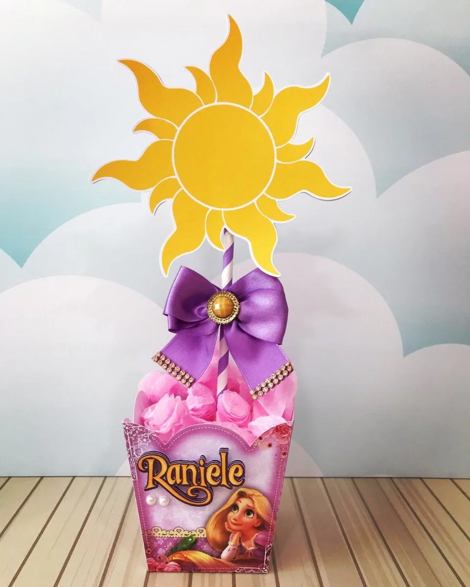 Centro de Mesa Rapunzel 1 Topo de bolo decorado com sol amarelo, laço roxo e ilustração feminina.