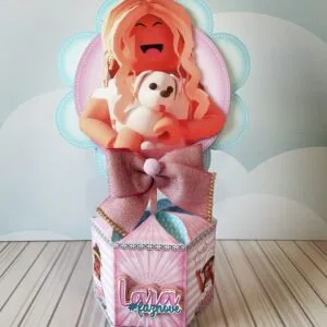 Topo de bolo decorativo rosa com personagem e laço brilhante em superfície listrada.