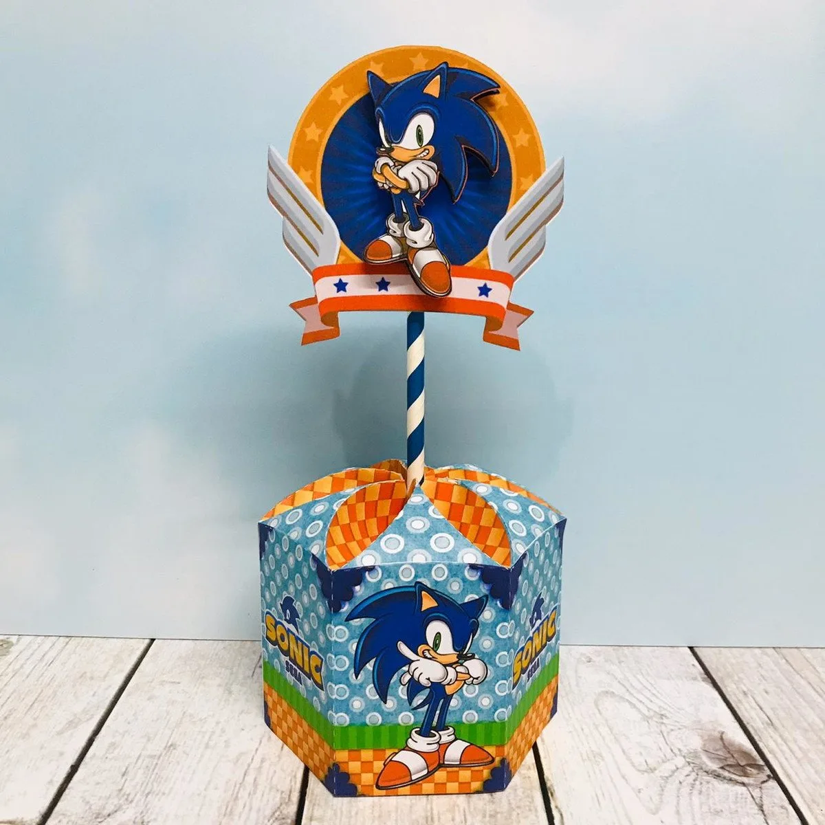 Topo de bolo com personagem azul de desenho animado sobre base hexagonal decorada.