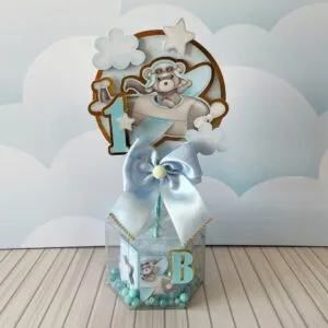 Decoração de mesa personalizada com urso aviador, laço azul e letras decorativas em caixa.