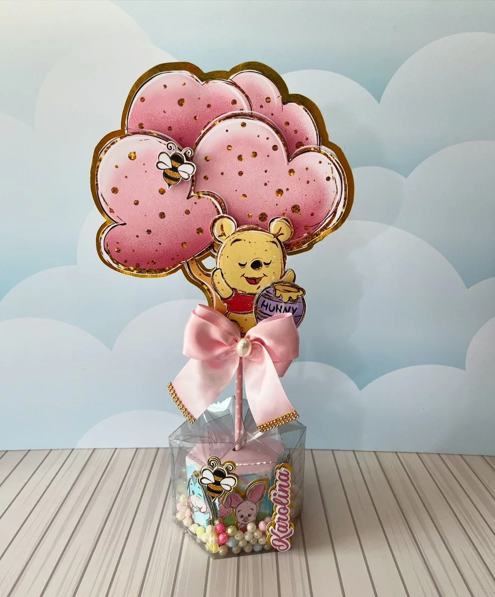 Topo de bolo decorativo com urso amarelo segurando balões em formato de coração.