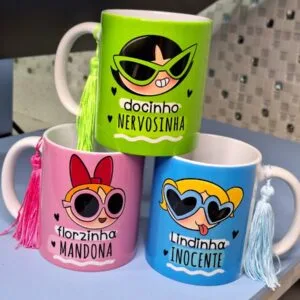 Três canecas coloridas decoradas com ilustrações de personagens femininas e pequenos pingentes decorativos.