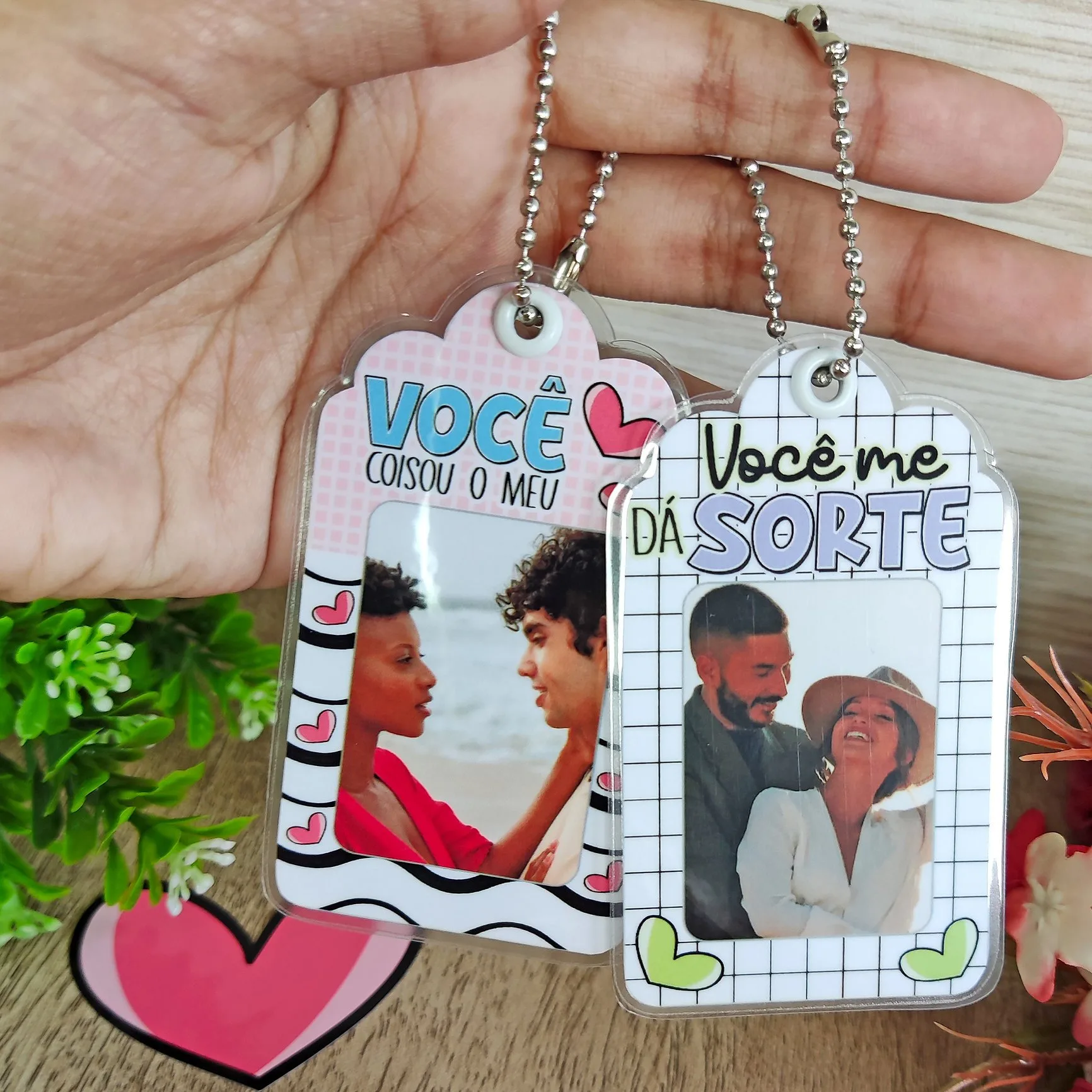 Mão segurando dois chaveiros com fotos e frases, flores e coração