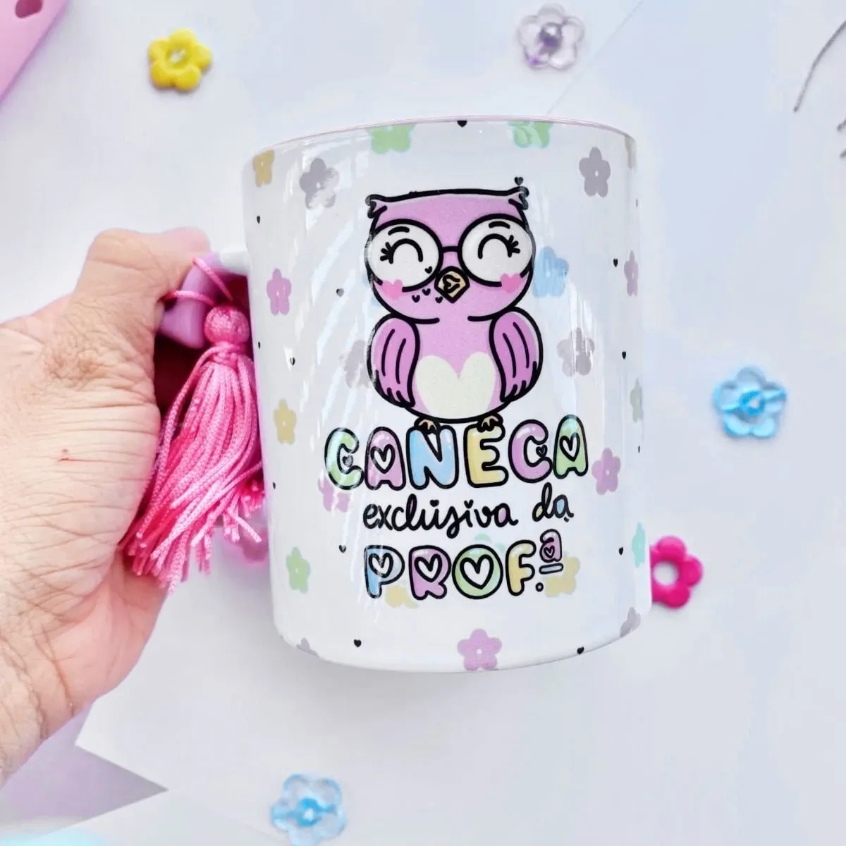 Mão segura caneca branca com coruja rosa, frase e borla rosa
