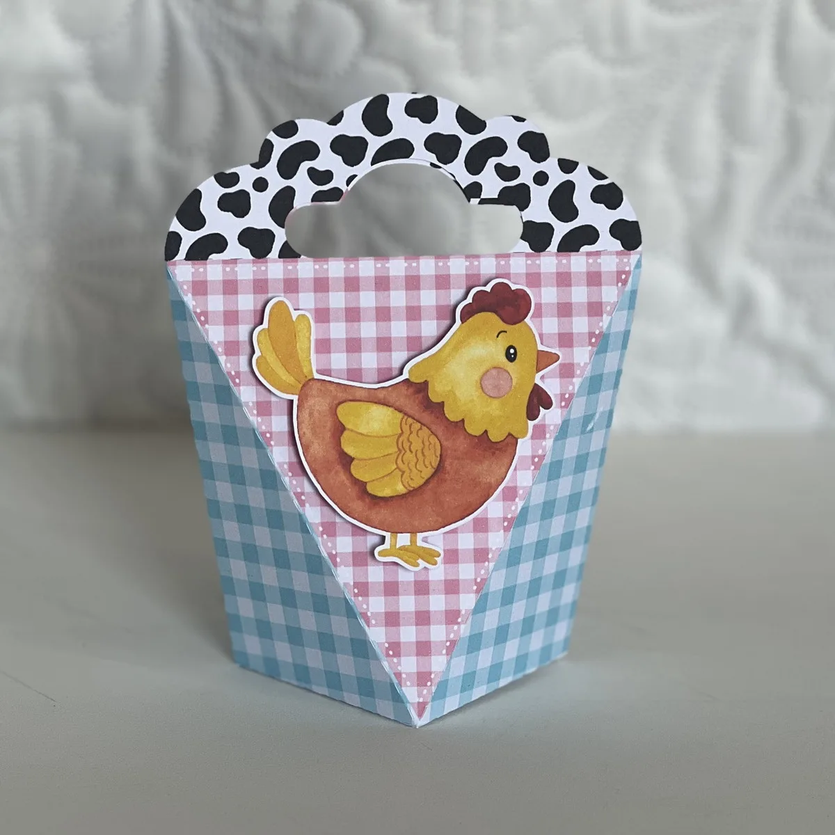 Caixinha de papel decorada com galinha cartoon, padrões xadrez e de vaca.