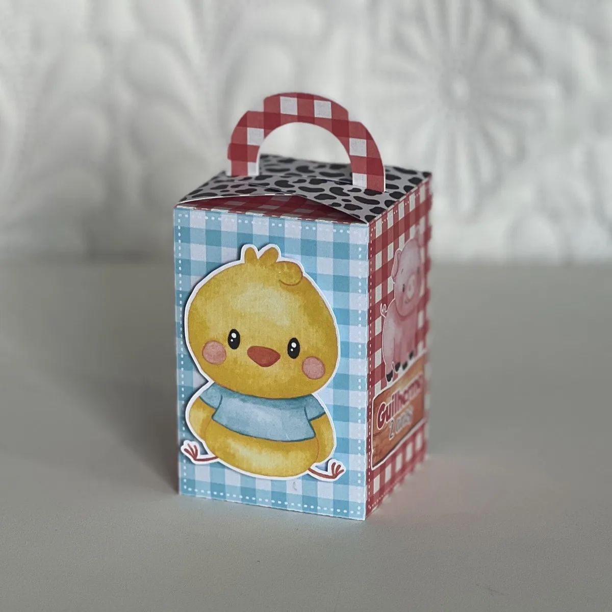Caixa de presente com pintinho amarelo, porco rosa e padrões diversos.
