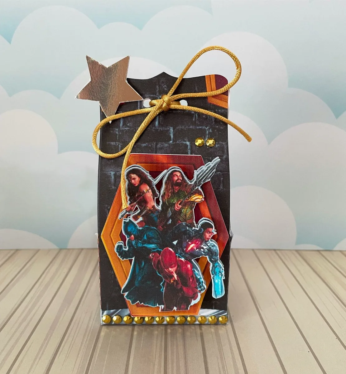 Kit Festa Liga da Justiça 4 Caixinha decorada com laço dourado e imagens de personagens heroicos em fundo azulado.