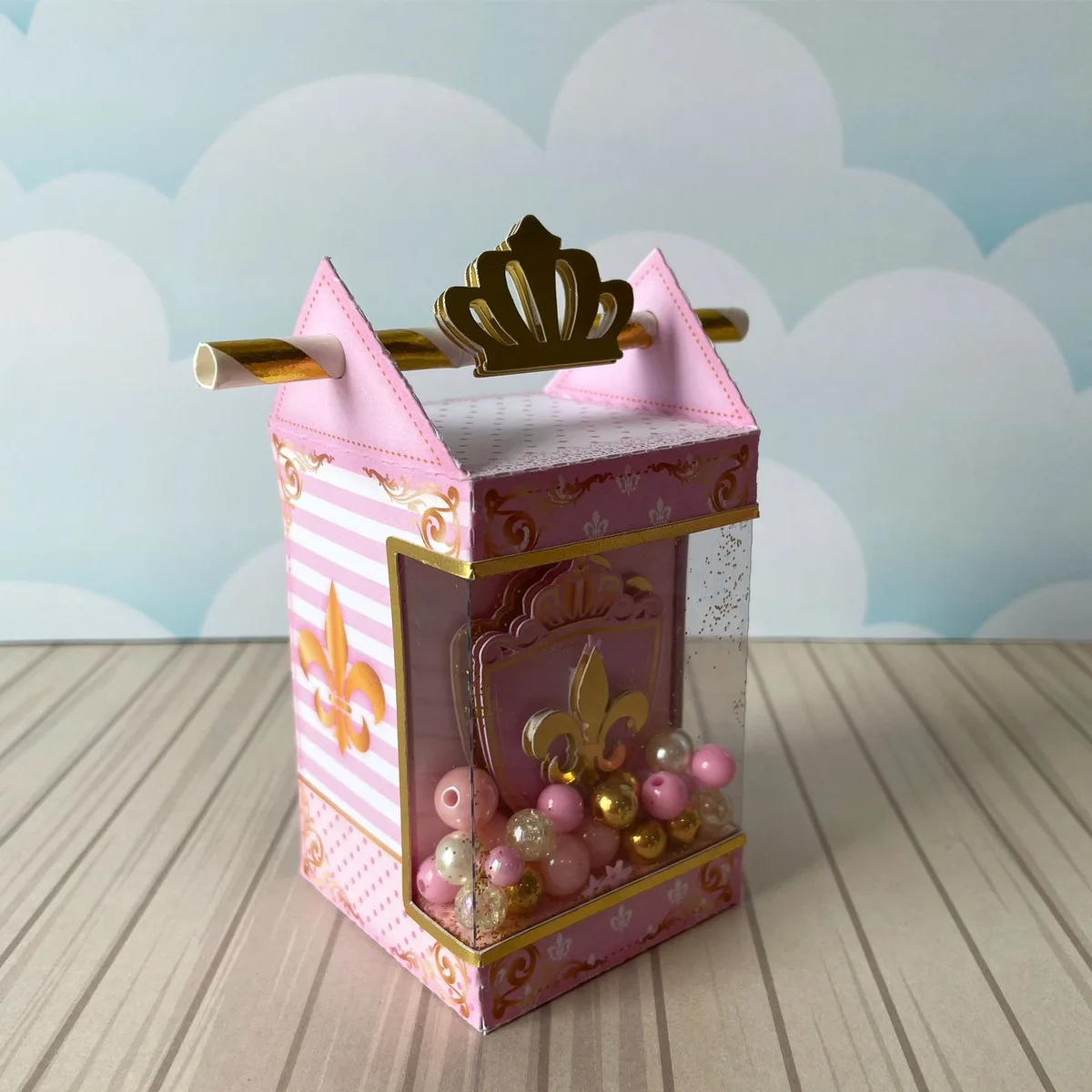 Kit Festa Realeza Menina 3 Caixa rosa de papel com coroa dourada e esferas coloridas na janela