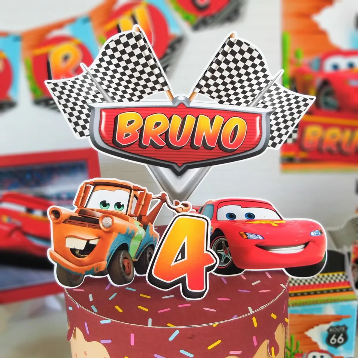 Topo de bolo temático com carros, bandeiras quadriculadas e o número quatro centralizado.