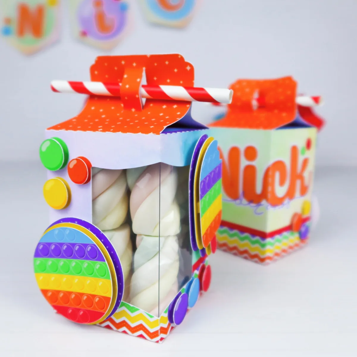 Duas caixinhas personalizadas coloridas contendo marshmallows com decoração temática festiva e lúdica.