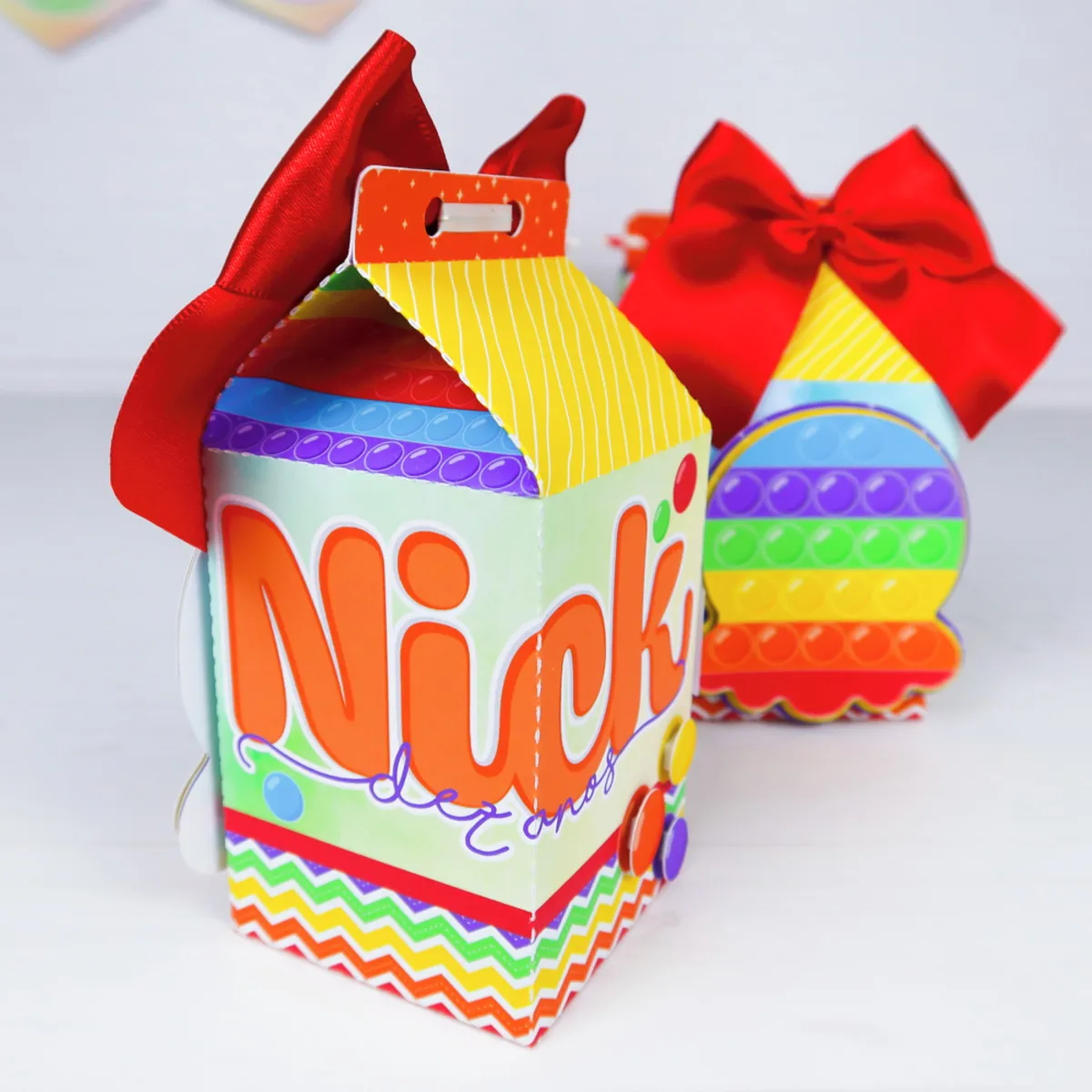Duas caixas personalizadas coloridas com laços vermelhos sobre um fundo branco liso.