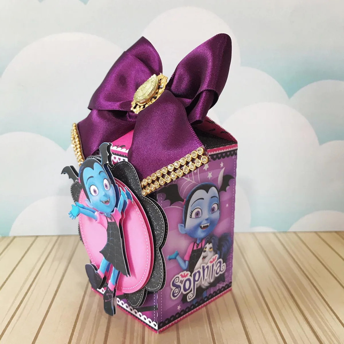 Caixa personalizada de papel decorada com laço roxo e personagem infantil de pele azul.
