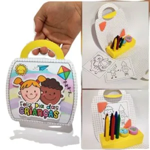 Maletinha Dia das Crianças - Studio e pdf 29 Mão segurando maleta de papel personalizada com tema infantil e itens de desenho.