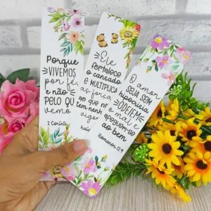 Marcadores de Bíblia 14 Mão segurando três marcadores de página decorados com flores, borboletas e mensagens religiosas escritas.