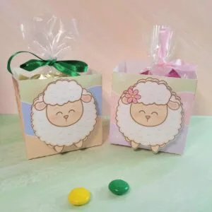 Mini Caixinha Aberta Páscoa 15 Duas caixas decoradas com ovelhas contêm sacos plásticos amarrados com fitas.