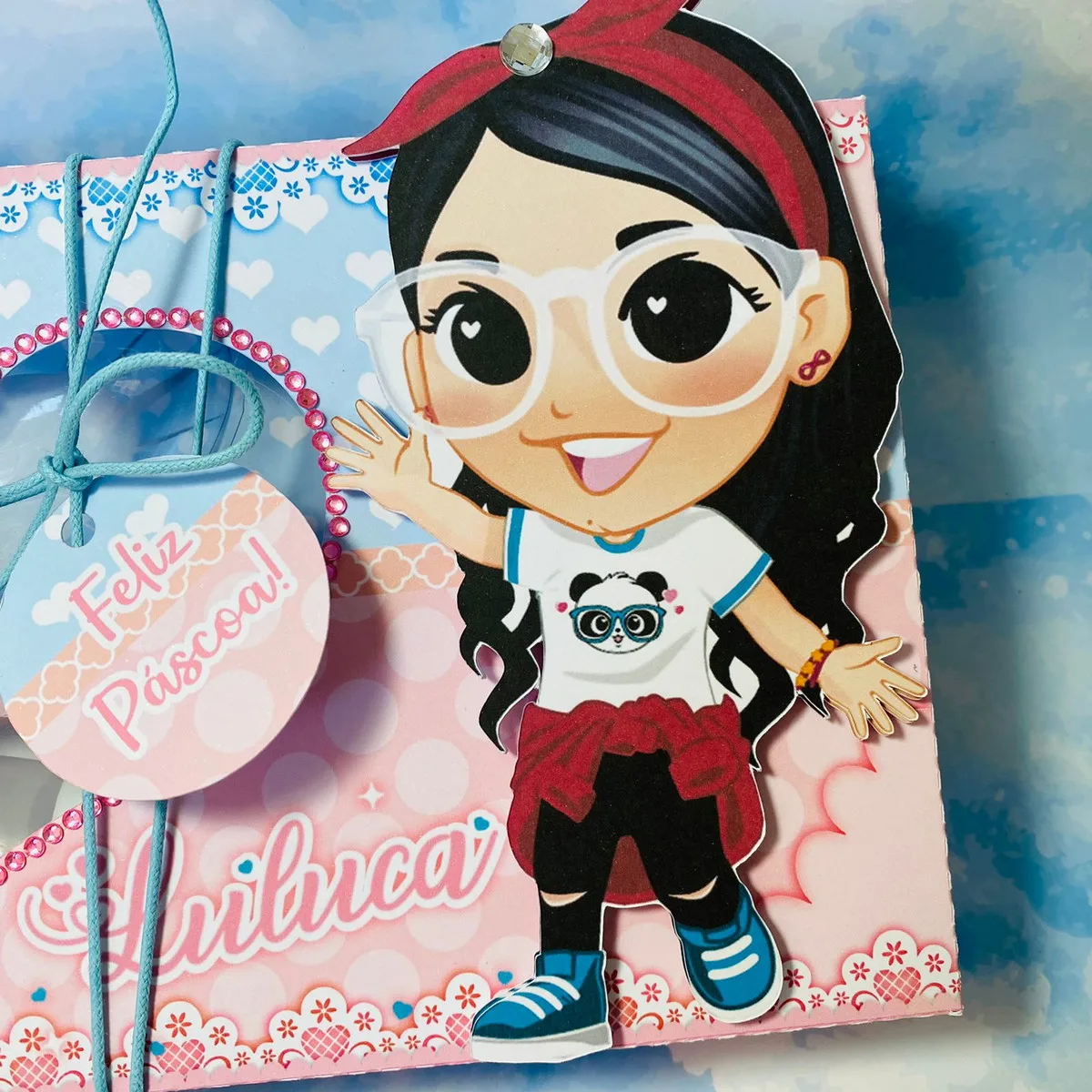 Mini Confeiteiro Luluca 3 Ilustração de menina com óculos, camisa branca e laço vermelho em caixa decorada.