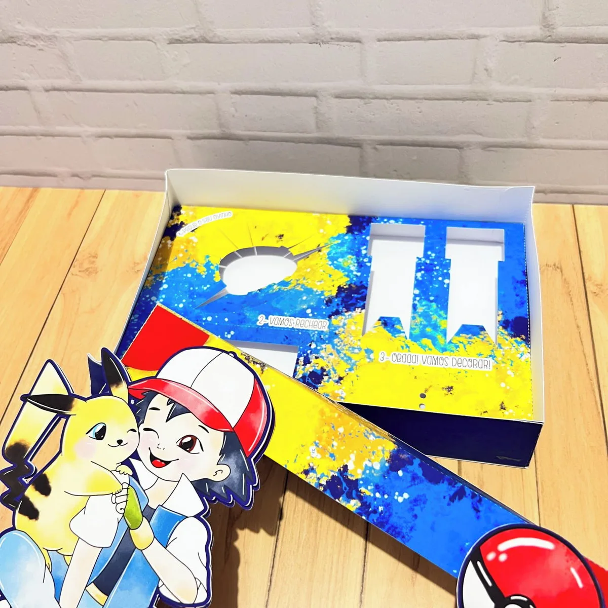 Mini Confeiteiro Páscoa Pokémon 2 Caixa de papelão aberta com impressões coloridas e recortes temáticos de desenho animado
