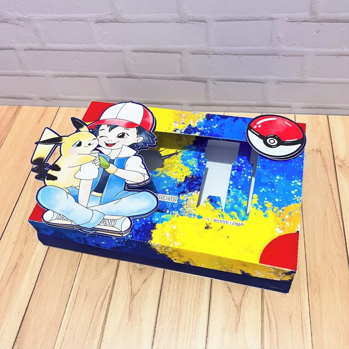 Mini Confeiteiro Páscoa Pokémon 1 Caixa colorida decorada com personagens infantis sobre uma mesa de madeira.