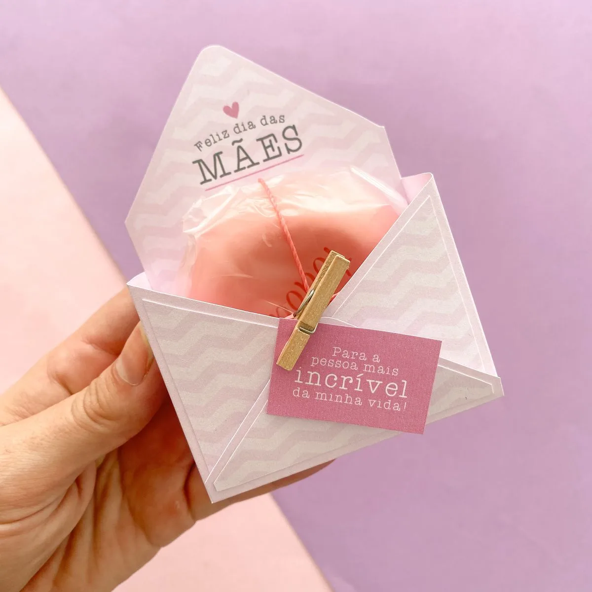 Mão segura envelope com mensagem de Dia das Mães e coração rosa