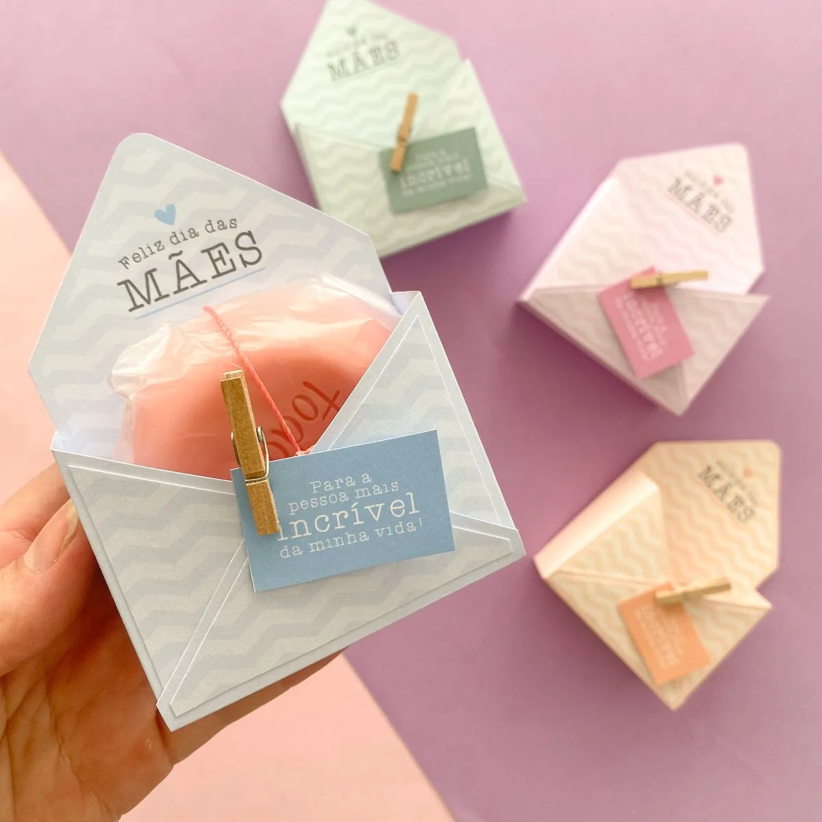 Mão segura envelope de papel com objeto rosa e etiqueta sobre fundo lilás