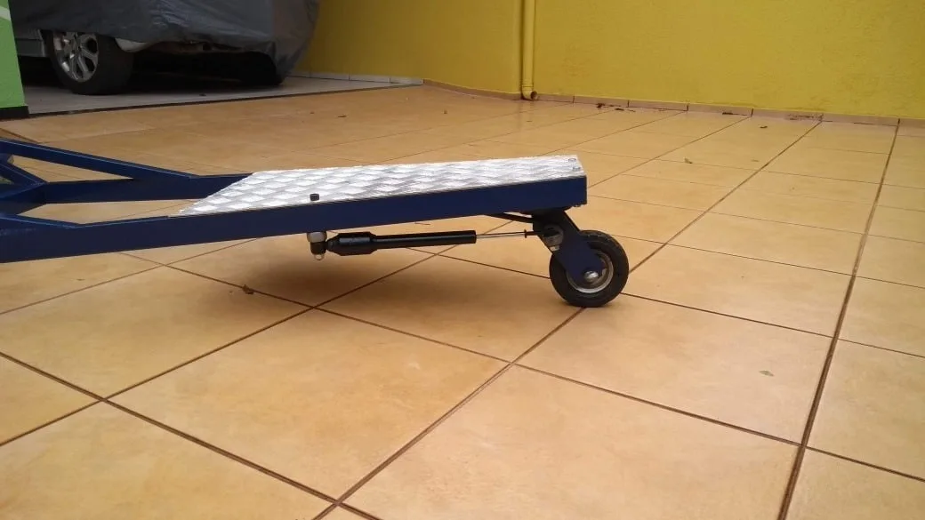 Estrutura metálica azul com plataforma xadrez e roda sobre piso de cerâmica.
