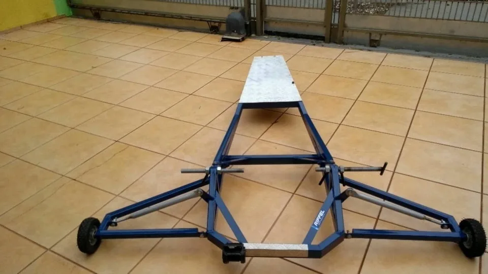 Estrutura tubular azul com rodas, plataforma branca e hastes sobre piso de cerâmica