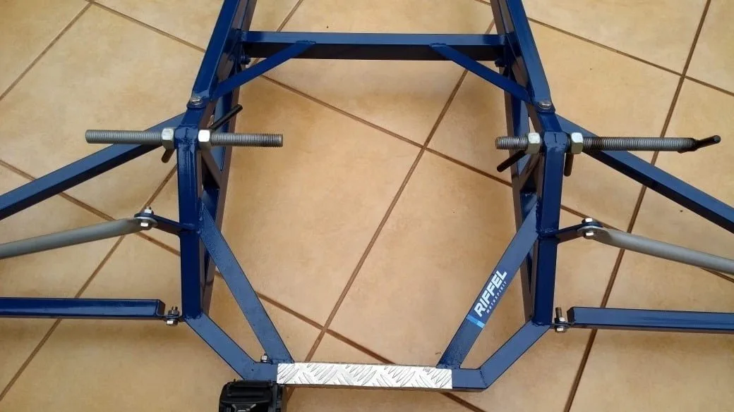 Estrutura metálica azul com hastes rosqueadas sobre piso de cerâmica.