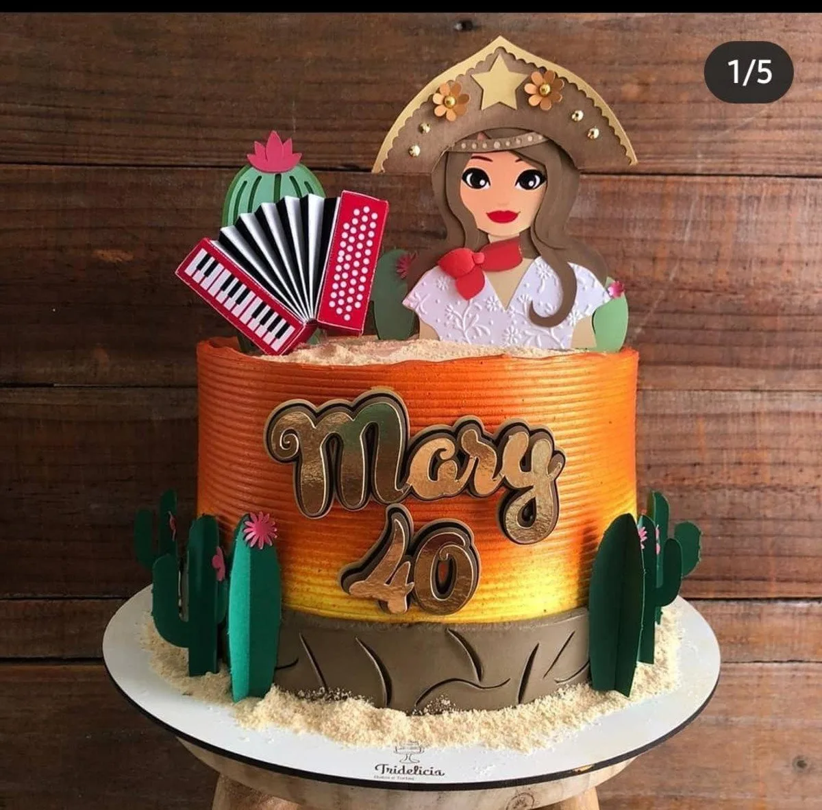 Bolo decorado com tema regional, cactos, sanfona, boneca de chapéu sobre fundo madeira.