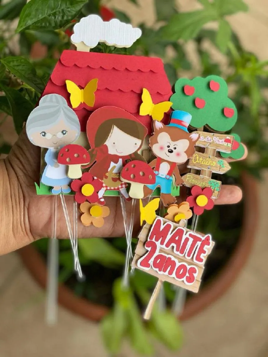 Topo de bolo de papel com personagens de conto infantil sobre fundo verde.